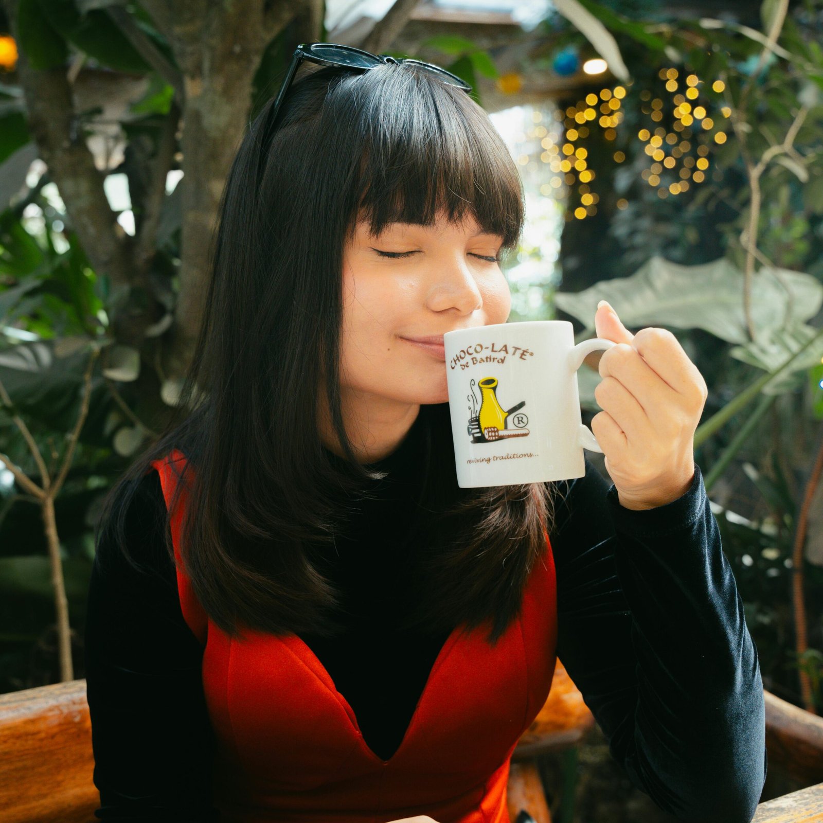 Woman in red dress savoring a hot drink outdoors in a cozy cafe setting.