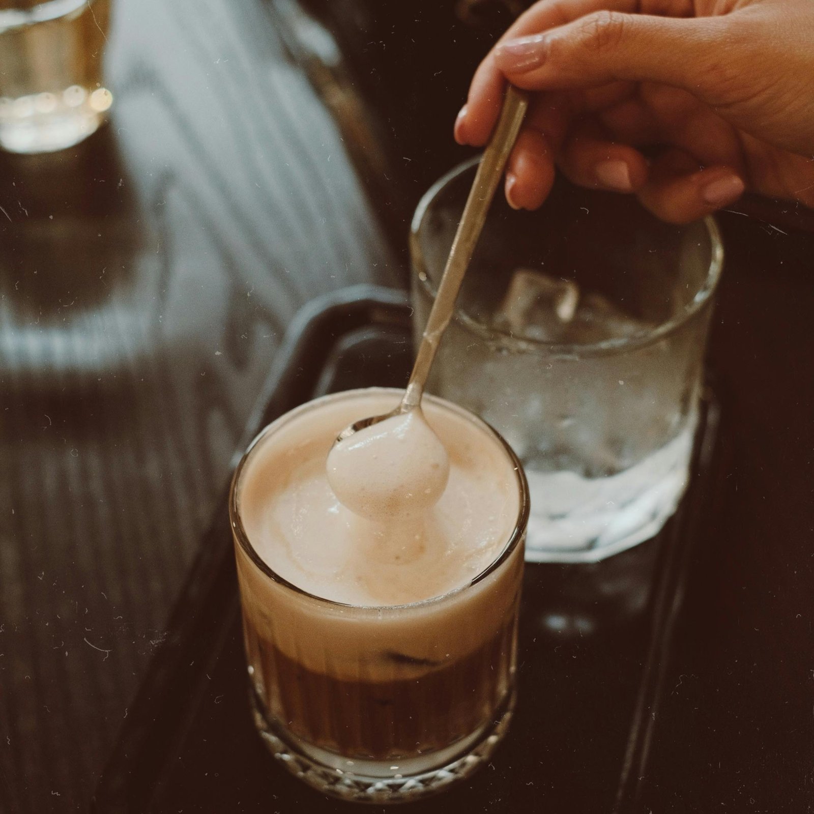 A hand stirs creamy coffee in a cozy setting, perfect for a warm, inviting atmosphere.