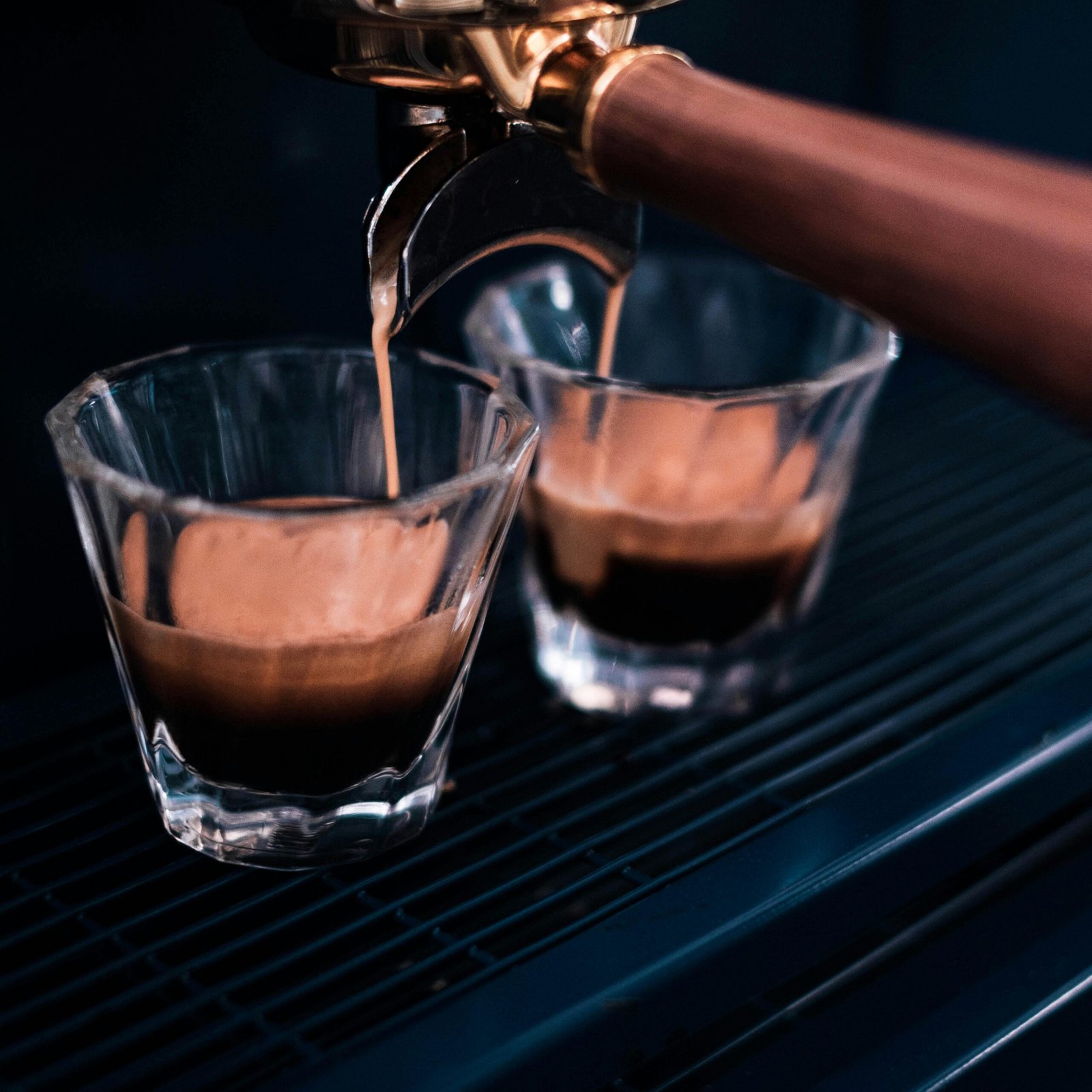 Close-up of espresso coffee flowing from a machine portafilter into glass cups, showcasing the crema and rich aroma.